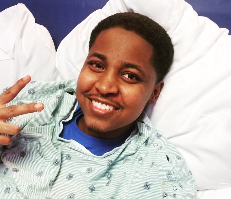 Qevonte smiling in a hospital bed, throwing up a peace sign
